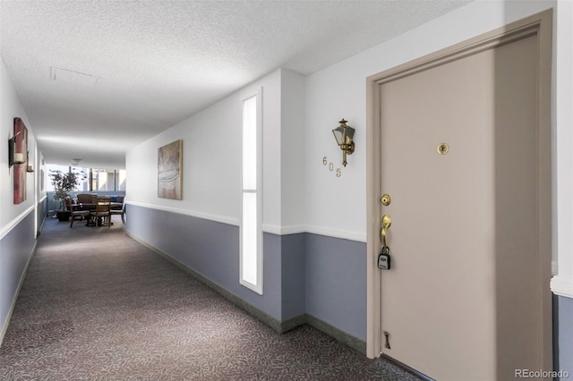 hallway with dark colored carpet and a textured ceiling