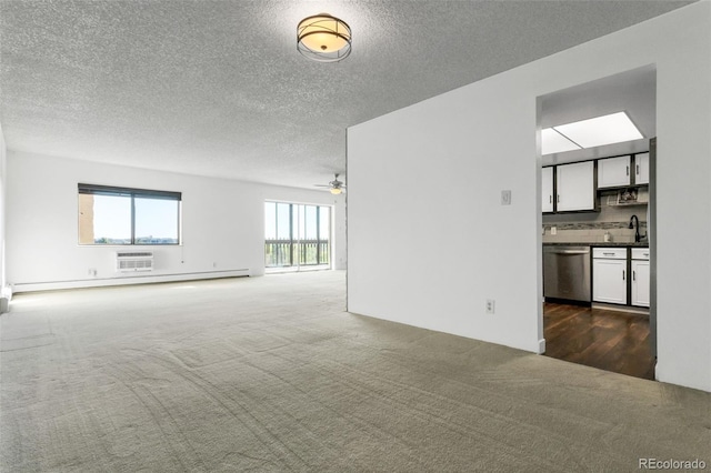 unfurnished living room with sink, ceiling fan, baseboard heating, dark colored carpet, and a textured ceiling