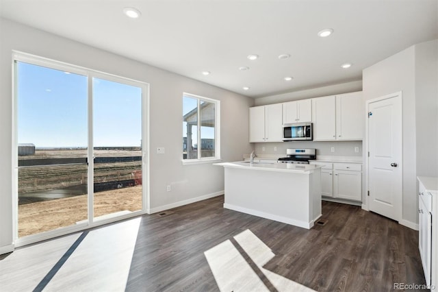 kitchen featuring stainless steel appliances, dark wood-type flooring, sink, a center island with sink, and white cabinets