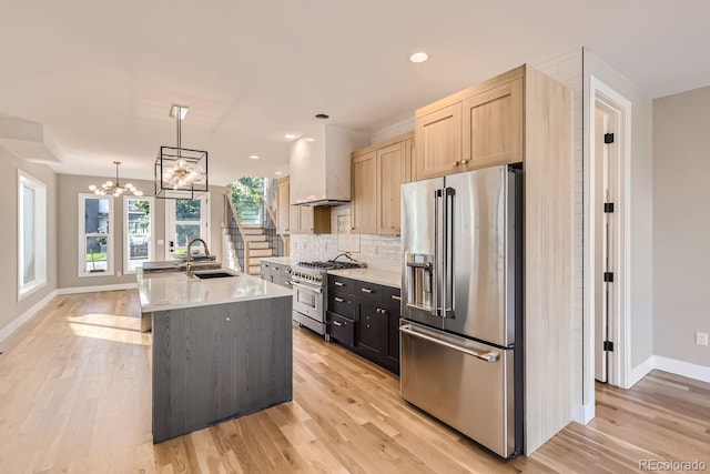 kitchen with custom exhaust hood, light brown cabinets, high end appliances, hanging light fixtures, and a kitchen island with sink