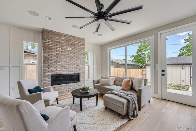 living room featuring a brick fireplace, light hardwood / wood-style flooring, and ceiling fan