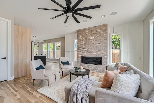 living room with light wood-type flooring, ceiling fan, and a fireplace