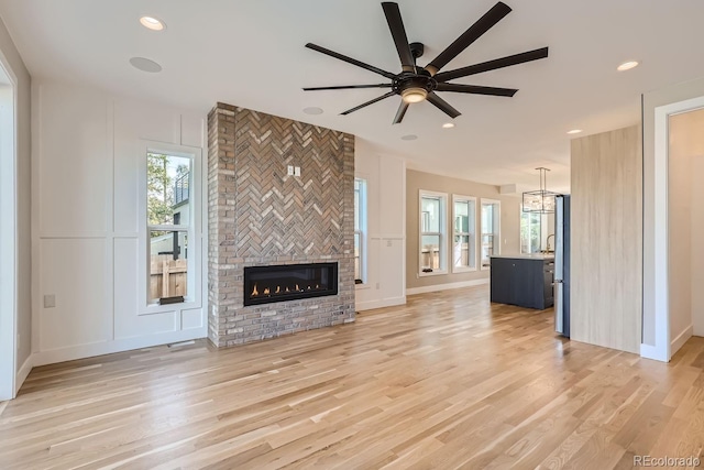 unfurnished living room featuring a fireplace, light hardwood / wood-style floors, and ceiling fan