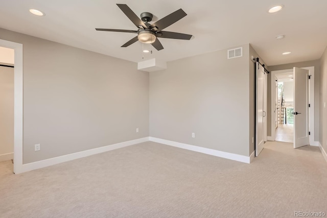 unfurnished bedroom featuring light carpet, ceiling fan, and a barn door