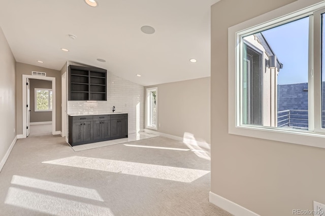 unfurnished living room featuring sink, vaulted ceiling, and light carpet