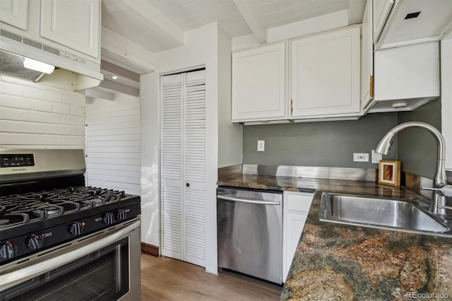 kitchen featuring beam ceiling, sink, stainless steel appliances, and white cabinetry