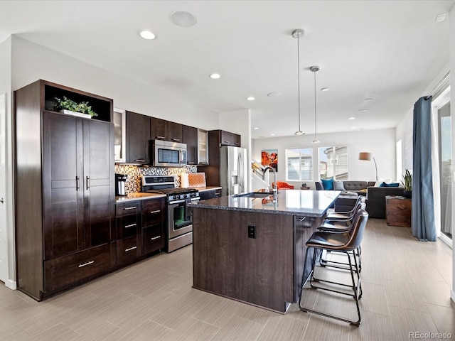 3368 Cranston Cir, Highlands Ranch, CO 80126 - kitchen with stainless steel appliances, dark brown cabinetry, a center island with sink, a kitchen bar, and decorative backsplash