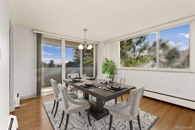 dining room featuring a healthy amount of sunlight, a baseboard radiator, wood-type flooring, and a chandelier