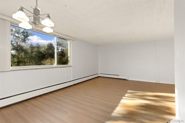 spare room with a baseboard heating unit, a healthy amount of sunlight, hardwood / wood-style floors, and an inviting chandelier