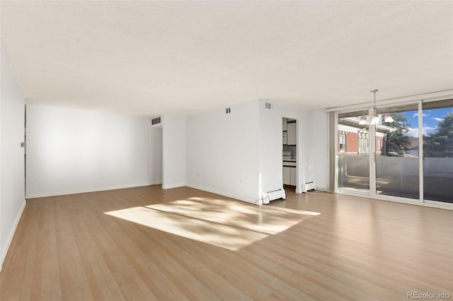 empty room featuring an inviting chandelier, expansive windows, a textured ceiling, a baseboard radiator, and light wood-type flooring