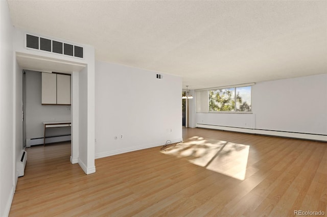 unfurnished room with visible vents, a baseboard heating unit, and wood finished floors