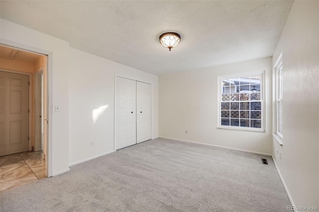 unfurnished bedroom featuring a closet, a textured ceiling, and light carpet