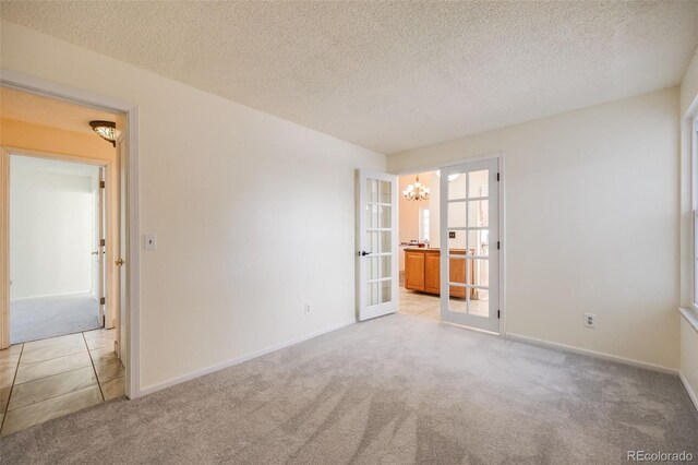 carpeted spare room featuring a textured ceiling, a notable chandelier, and french doors