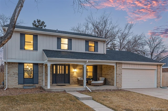 view of front of property with driveway, a porch, brick siding, an attached garage, and a front yard