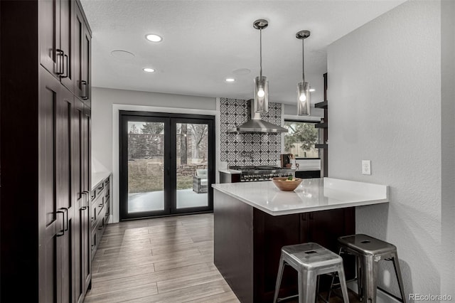 11861 E Yale Ct, Aurora, CO 80014 - kitchen with wall chimney exhaust hood, a breakfast bar, light countertops, dark brown cabinetry, and recessed lighting