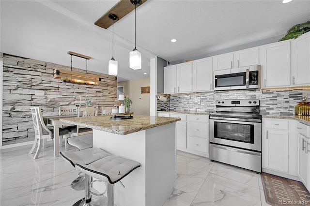 kitchen featuring appliances with stainless steel finishes, white cabinetry, hanging light fixtures, a kitchen breakfast bar, and a center island