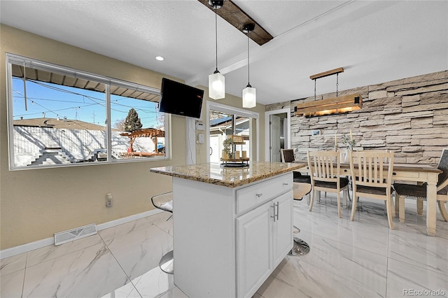 kitchen with white cabinetry, decorative light fixtures, a center island, a textured ceiling, and light stone countertops