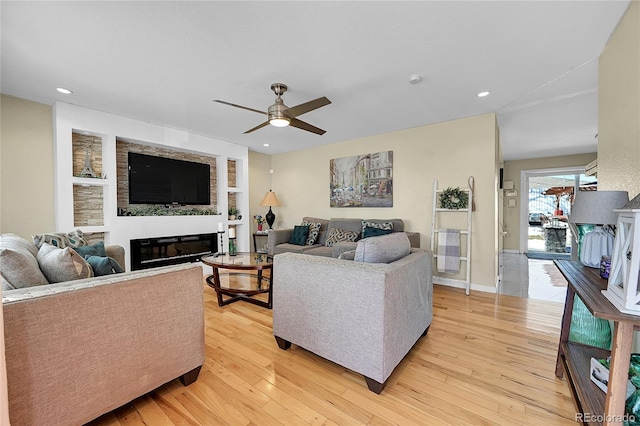 living room featuring light hardwood / wood-style flooring, a large fireplace, and ceiling fan