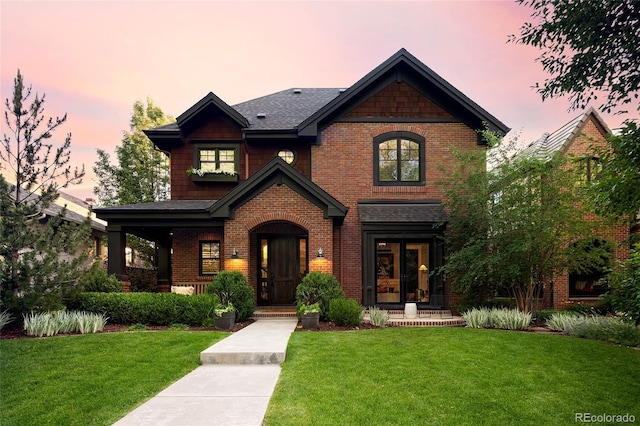 view of front of home featuring french doors, brick siding, and a lawn