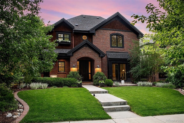 view of front of home featuring a front yard, brick siding, and roof with shingles