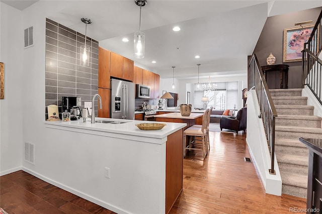 kitchen featuring sink, a kitchen breakfast bar, light hardwood / wood-style flooring, kitchen peninsula, and appliances with stainless steel finishes