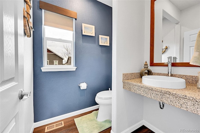 half bathroom with baseboards, visible vents, toilet, wood finished floors, and a sink