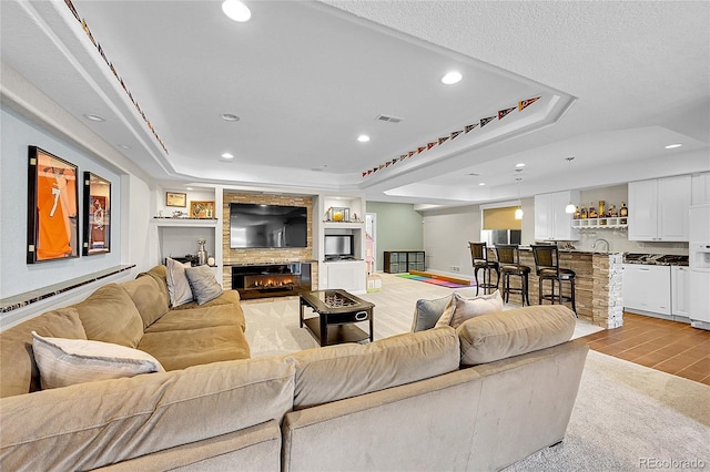 living room with recessed lighting, wood finish floors, visible vents, a tray ceiling, and a glass covered fireplace