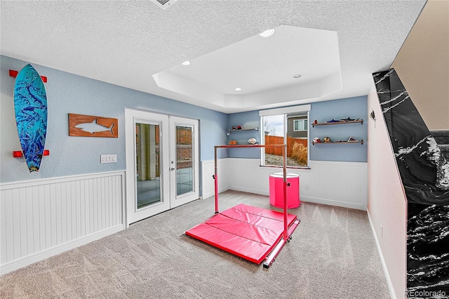 carpeted bedroom with french doors, a raised ceiling, a wainscoted wall, and a textured ceiling