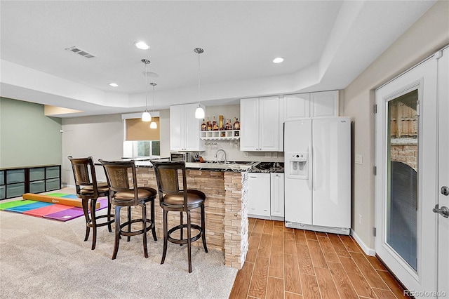 kitchen featuring white refrigerator with ice dispenser, visible vents, white cabinetry, hanging light fixtures, and light wood finished floors