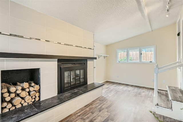 unfurnished living room featuring light hardwood / wood-style flooring, vaulted ceiling, a textured ceiling, and a tile fireplace