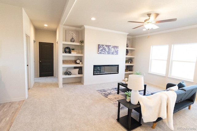 carpeted living room with built in shelves, ceiling fan, and crown molding