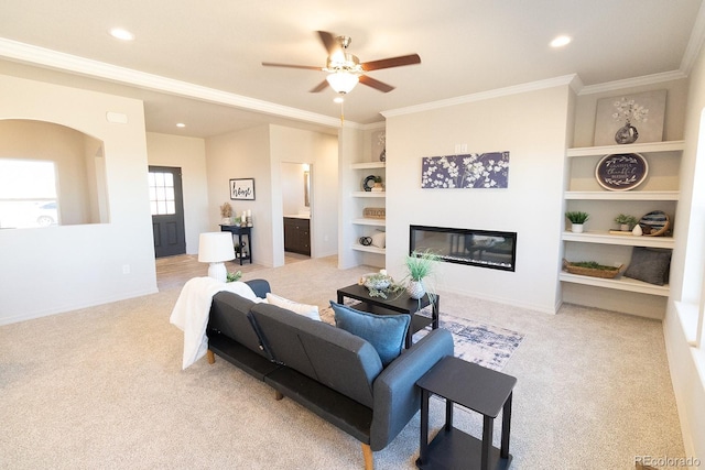 carpeted living room featuring built in shelves, ceiling fan, and crown molding