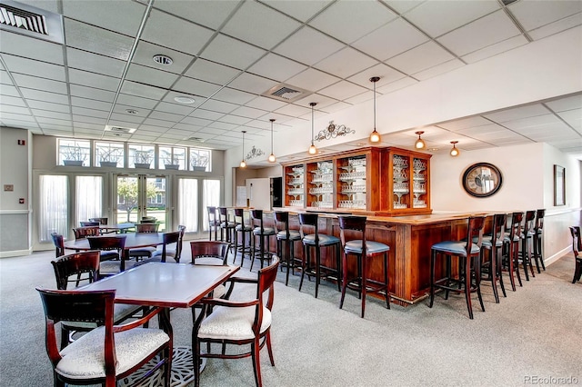 dining area with bar area, a paneled ceiling, french doors, and light colored carpet