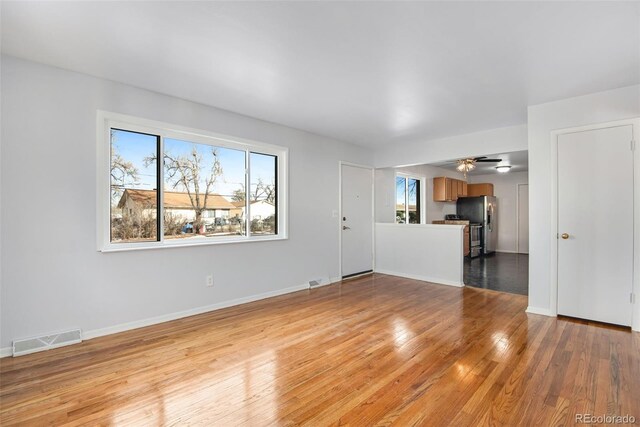 unfurnished living room with a ceiling fan, baseboards, light wood-type flooring, and visible vents