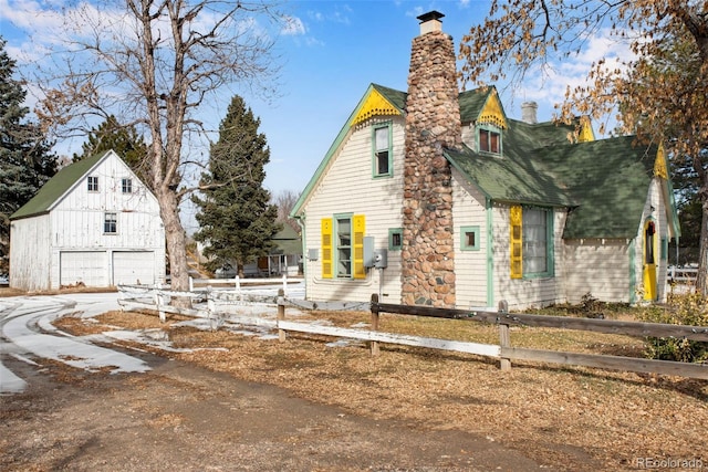 view of side of home with a chimney, fence, an outbuilding, roof with shingles, and a detached garage