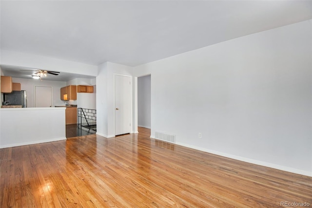 unfurnished living room featuring baseboards, a ceiling fan, visible vents, and light wood-style floors