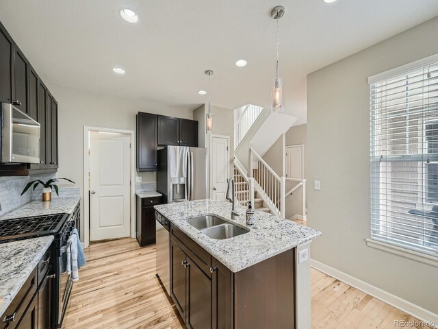 kitchen with sink, decorative light fixtures, a center island with sink, stainless steel appliances, and decorative backsplash