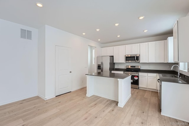 kitchen with sink, a center island, light wood-type flooring, appliances with stainless steel finishes, and white cabinets