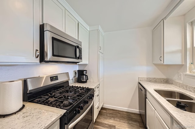 kitchen featuring stainless steel appliances, a sink, dark wood finished floors, light stone countertops, and baseboards