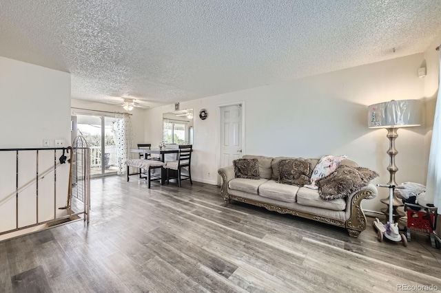 living room with a textured ceiling, wood finished floors, ceiling fan, and baseboards
