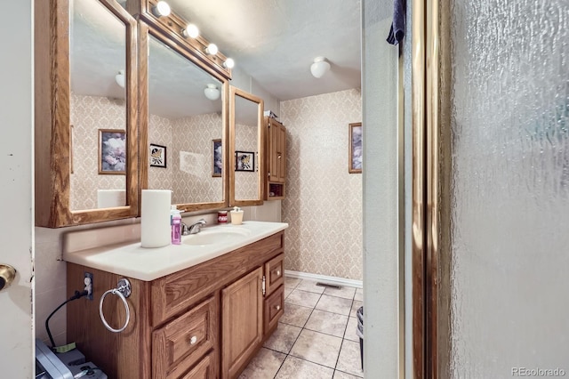 bathroom with wallpapered walls, tile patterned flooring, vanity, and baseboards