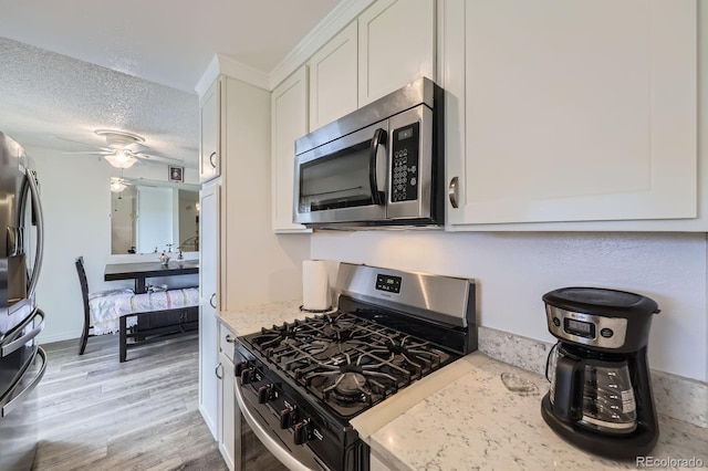 kitchen featuring appliances with stainless steel finishes, white cabinets, light wood-type flooring, a textured ceiling, and light stone countertops