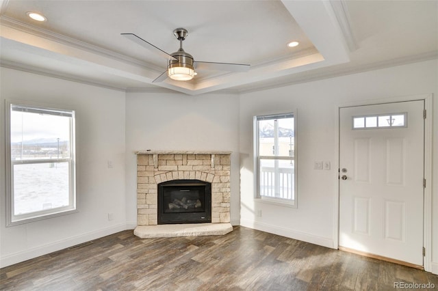 unfurnished living room with ceiling fan, dark wood-type flooring, a raised ceiling, a fireplace, and ornamental molding