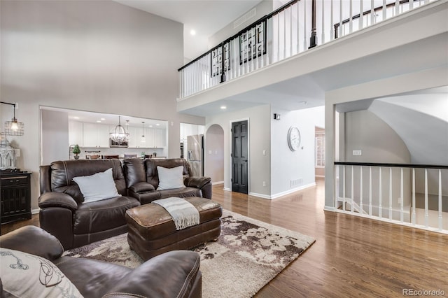 living area with a high ceiling, wood finished floors, a chandelier, baseboards, and arched walkways