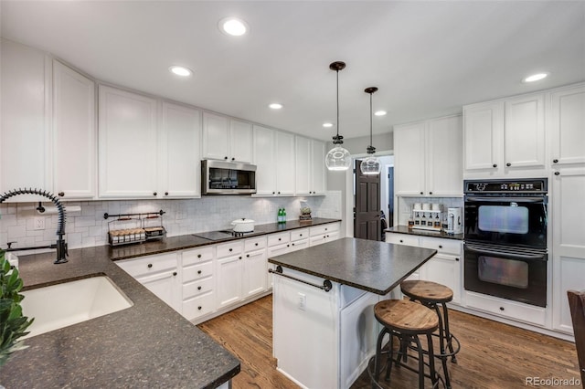 kitchen with black appliances, a sink, decorative backsplash, a breakfast bar area, and white cabinets