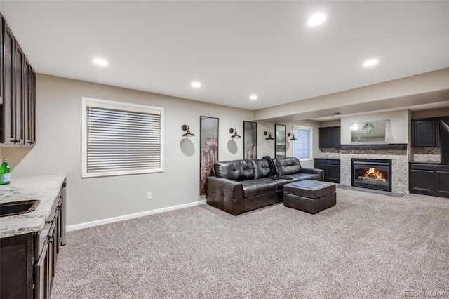 carpeted living room featuring baseboards, a glass covered fireplace, recessed lighting, and a sink