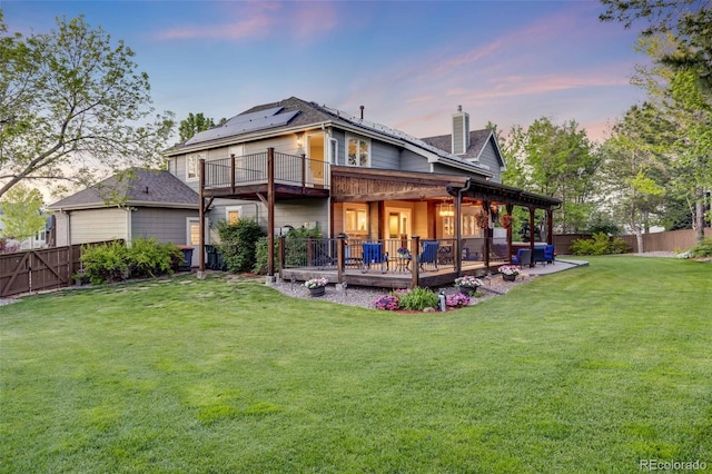 back of property at dusk with a chimney, roof mounted solar panels, and a wooden deck