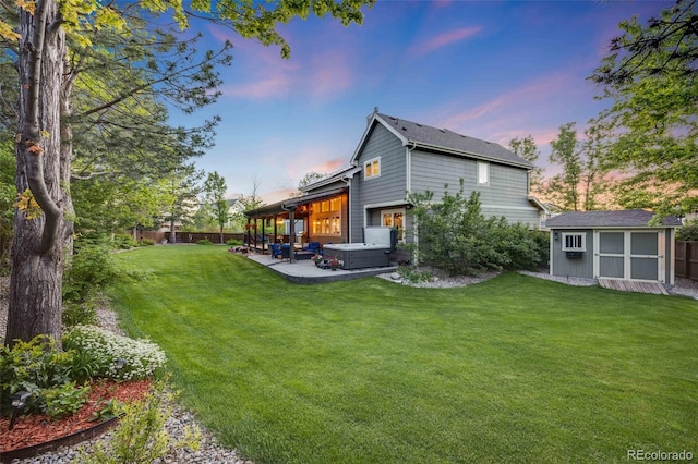 back of property at dusk featuring a hot tub, a patio area, an outbuilding, and a shed