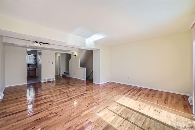 empty room with light wood-style floors, baseboards, stairs, and visible vents