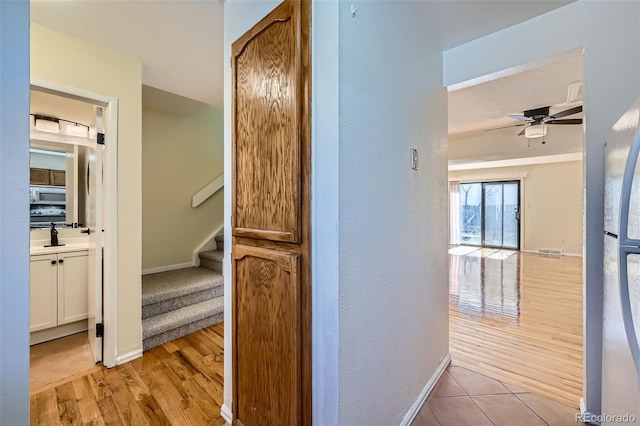 hallway featuring light wood finished floors, baseboards, stairs, and visible vents